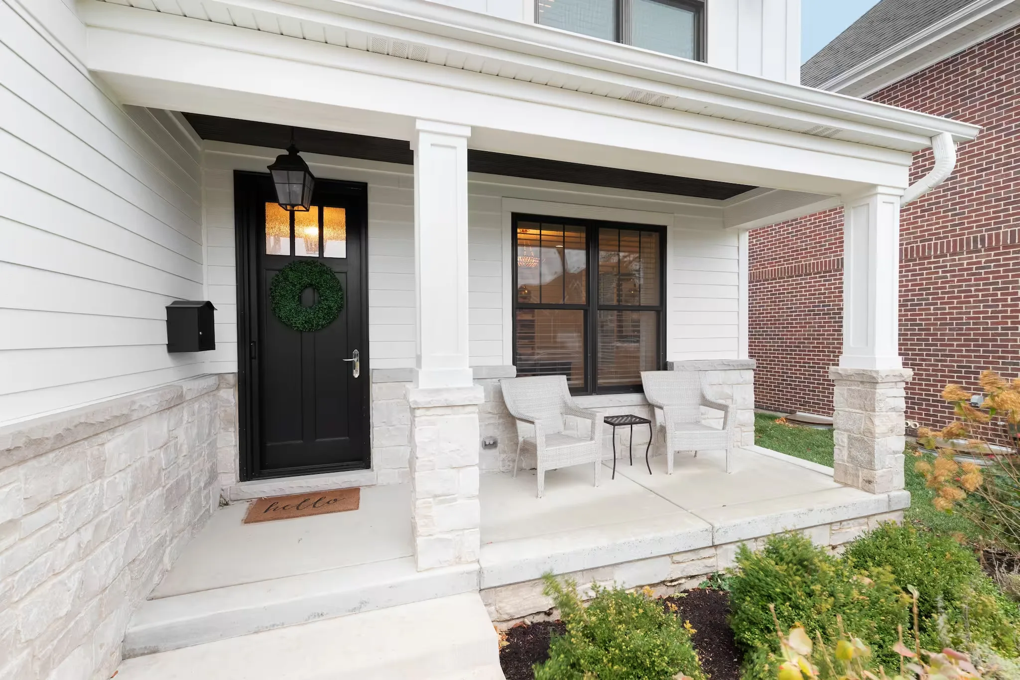 White porch with a black entry door, a wreath and a lantern beside a large window