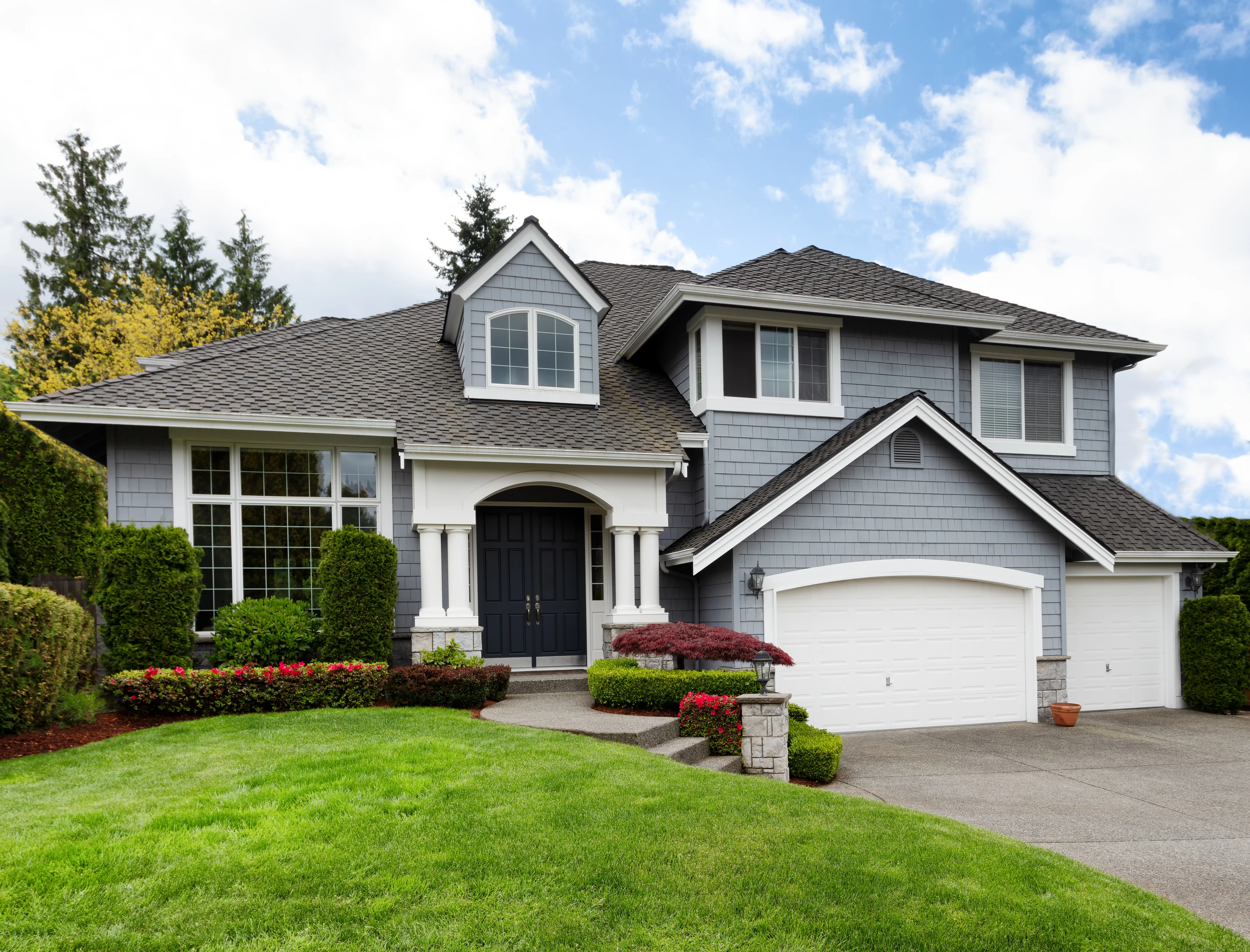 Gray two-story home with white trim, an arched front entry and a two-car garage behind a green lawn