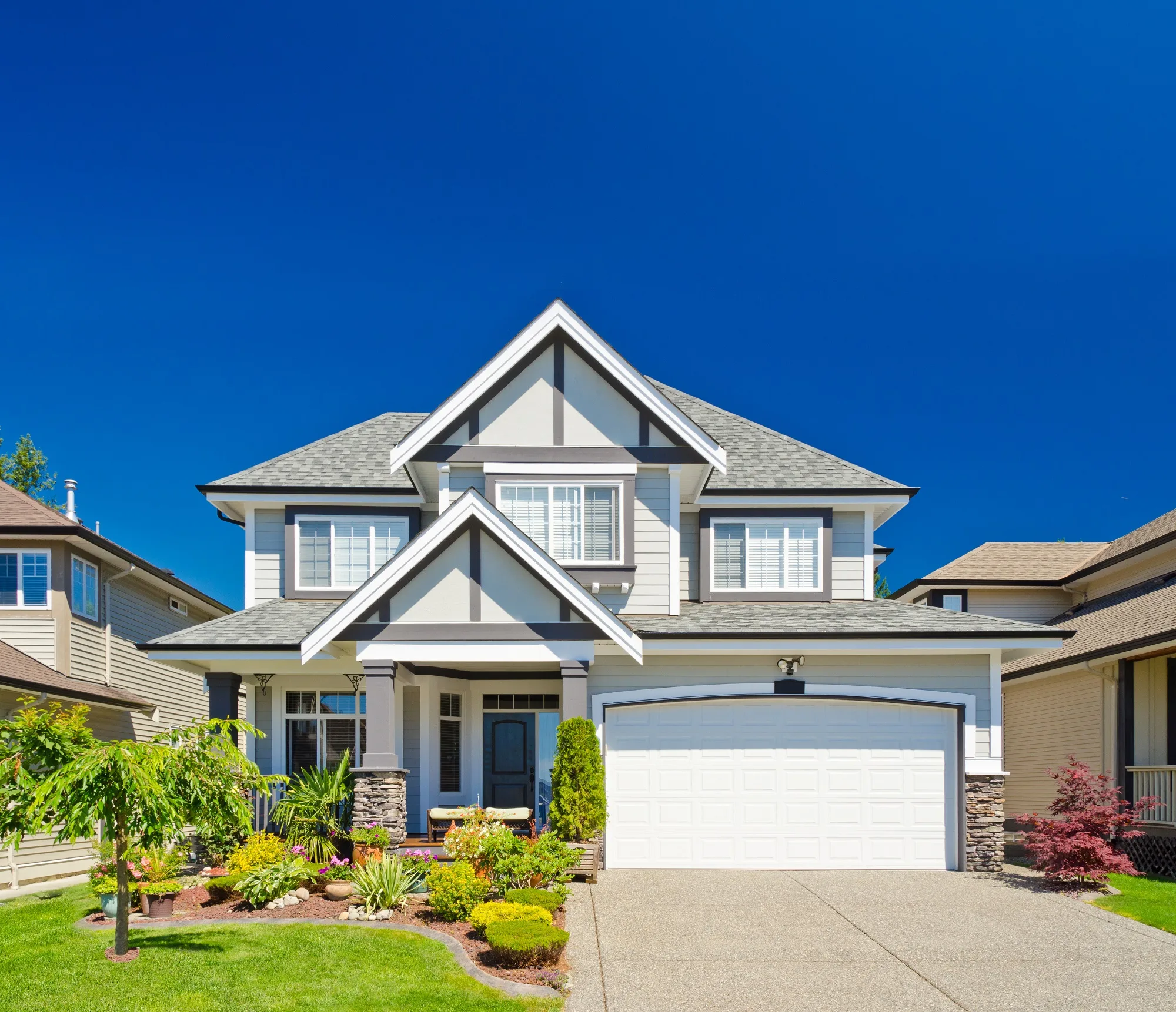 Two-story gray house with white trim, gabled roof and a white garage door under a clear blue sky