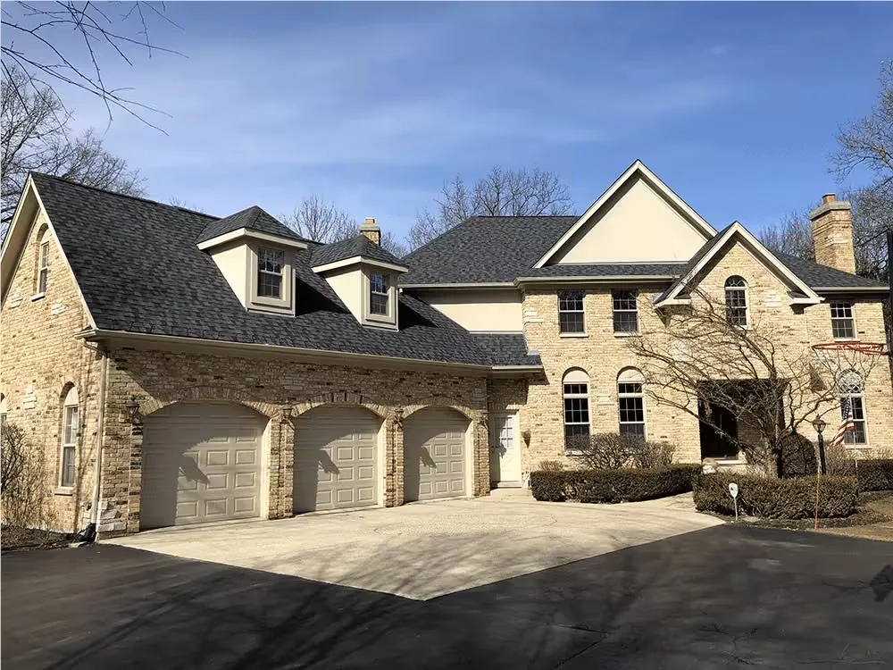 Stone-clad two-story house with a dark architectural shingle roof and dormers