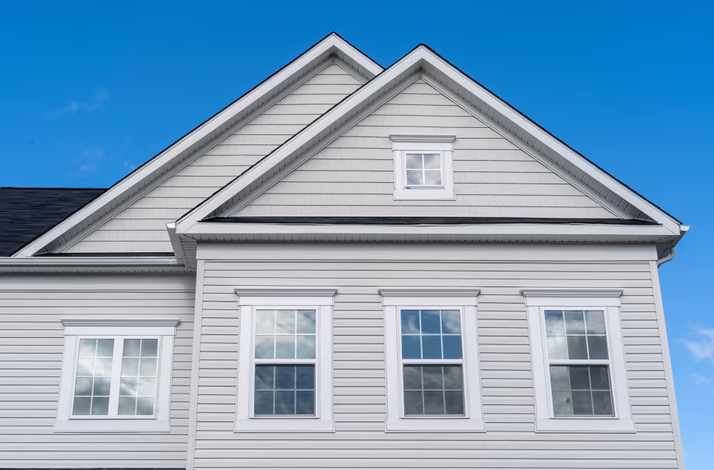 House gables with light vinyl siding and white double-hung windows with grids under a blue sky