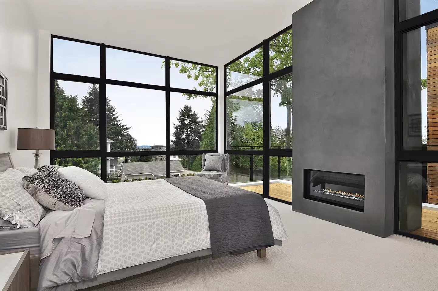 Bedroom with floor-to-ceiling black-framed windows looking out on trees